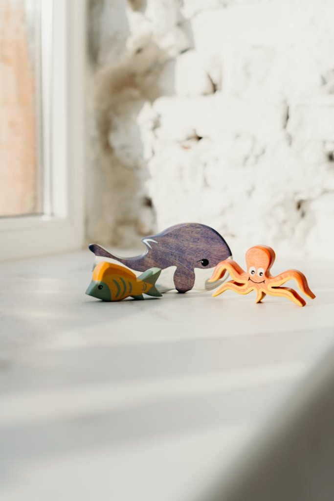 Vibrant wooden ocean animal toys, including a fish and octopus, bathed in sunlight on a windowsill.